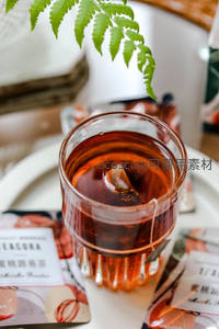 玻璃杯中冰红茶配茶包标签，蕨叶轻垂营造清新茶饮氛围
