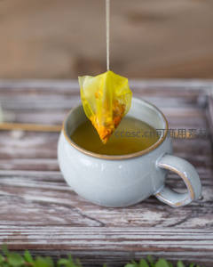 黄透茶包悬垂入杯：古朴陶杯中的花果茶萃取特写