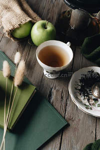 木质桌面上茶杯配青苹果与干草书本，复古茶具演绎森系生活
