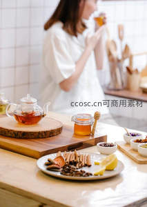 厨房中女子品饮花果茶，前景陈设蜂蜜、肉桂与柠檬片营造温馨氛围