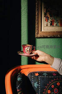 手托复古彩绘茶杯，绿墙光影交织的静谧午后时光