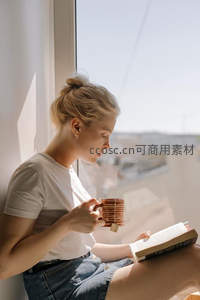 窗边阅读时光：金发女子手捧陶杯静享书香与阳光