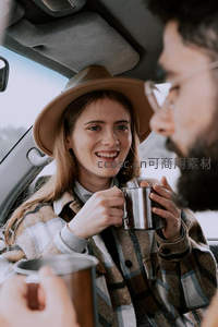 车内微笑女子持金属杯对视交谈，冬日旅行途中温暖瞬间