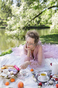 粉纱裙女子卧于湖畔野餐垫，手触精致茶点，春日花园午后诗意场景