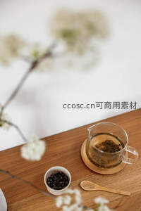 微距视角下茶席一角：玻璃公道杯、干茶粒与虚化梨花枝