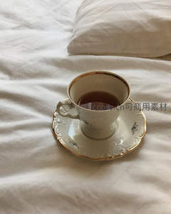 复古金边瓷杯置于素雅床单上，晨光中的宁静茶时光
