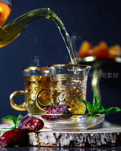 金色雕花玻璃杯中热茶倾泻，搭配椰枣与薄荷叶的异域风情茶饮