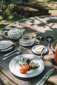 户外石桌早餐布景：班尼迪克蛋、手绘茶壶与自然光影