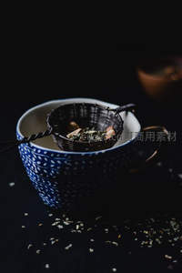 青花瓷杯中茶滤静置，散落茶叶点缀暗调雅致茶道场景
