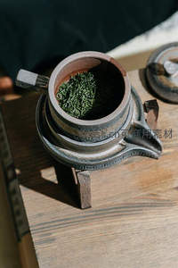 古朴陶壶中盛放新采绿茶，阳光洒落显茶芽鲜嫩翠绿