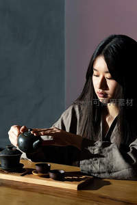 女子专注冲泡黑陶茶具，光影交错间展现东方茶道静谧之美