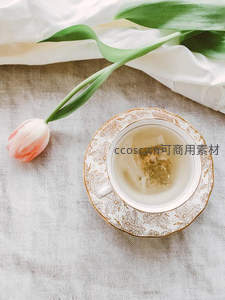 白瓷茶杯中泡着茶包，旁置粉白郁金香与亚麻布，静谧雅致