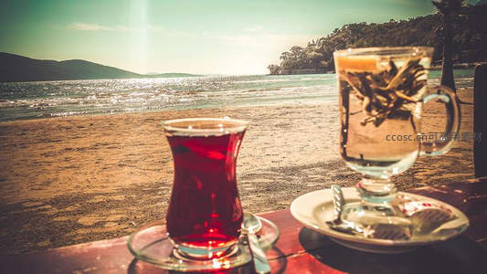 海滩木桌上的土耳其红茶与透明花茶杯，远山碧海为背景，度假风情浓郁