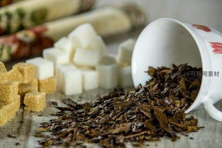 散落的干茶叶与白砂糖、红糖块，陶瓷杯倾倒静物特写