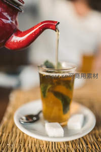 红釉茶壶倾注薄荷茶入玻璃杯的动态瞬间