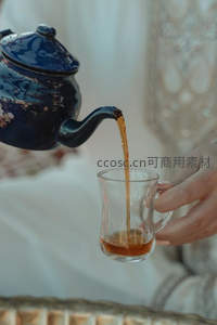 深蓝釉瓷壶倾注琥珀茶汤，手握透明玻璃杯承接温润瞬间