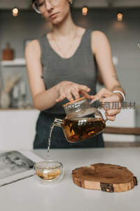 玻璃茶壶倾注琥珀茶汤：女子专注泡茶的静谧瞬间