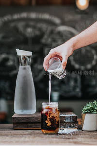 手正将牛奶倒入冰美式咖啡中，形成乳白漩涡特写