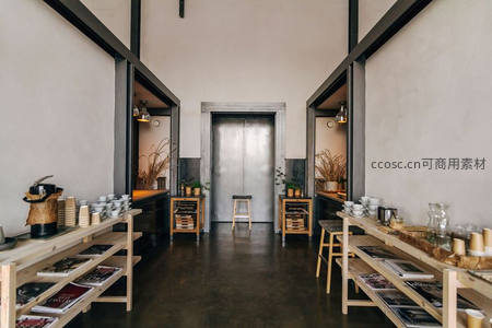 工业风咖啡馆长廊式空间，原木货架陈列杯具与杂志，中央金属门与绿植点缀