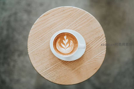 俯拍木质圆桌上精致拉花咖啡杯特写