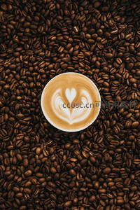 心形拉花艺术咖啡置于深烘咖啡豆海中，俯拍构图展现视觉美感