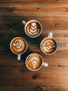 四杯拉花咖啡摆于原木桌面，叶形奶泡艺术精致对称