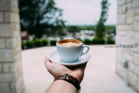 手托蓝白咖啡杯，石柱廊道外绿意朦胧的午后时光