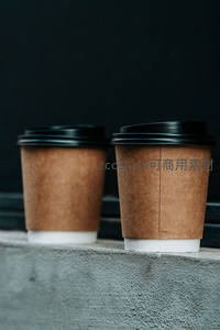 两杯环保纸杯咖啡静置于灰色水泥台面，深色背景衬托简约质感