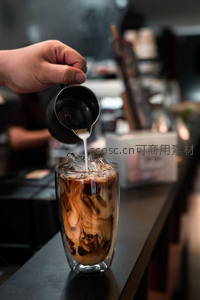 咖啡师在吧台现场制作冰拿铁：牛奶注入双层玻璃杯