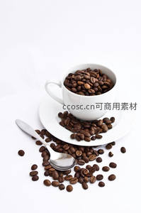 白瓷杯盛满深烘咖啡豆，散落于碟与桌面，银勺静置旁侧