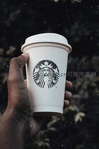 手持星巴克纸杯特写，雨滴背景下的经典品牌标识