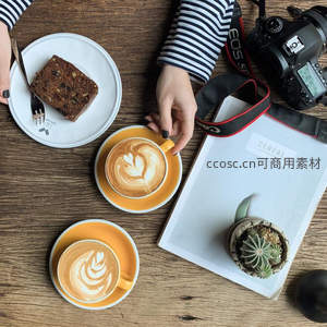 条纹衫女子手握拉花咖啡杯，桌上书本、多肉与蛋糕构成静谧下午茶构图