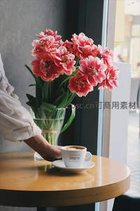 窗边手握咖啡杯，粉色郁金香映衬都市咖啡馆午后时光