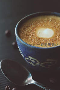 蓝釉陶杯中的拿铁咖啡特写，奶泡细腻，咖啡豆点缀暗色背景