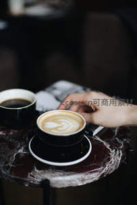 大理石桌上的手握拉花咖啡杯，背景虚化营造静谧氛围