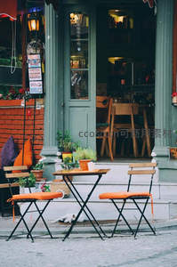 绿门咖啡店外景，橙色折叠椅与慵懒猫咪构成街角诗意