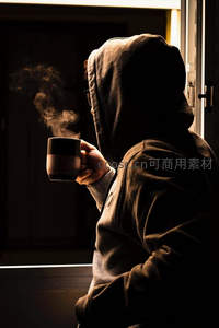 逆光中戴帽青年手持热咖啡，蒸汽袅袅升腾