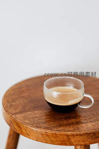 透明玻璃咖啡杯盛意式浓缩置于原木圆凳，光影层次丰富