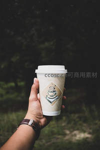 手持纸杯咖啡于林间，简约logo映衬自然光影