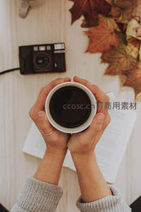 双手捧杯阅读时光，复古相机与秋叶点缀木质书桌