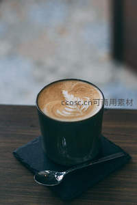 黑瓷杯中叶形拉花咖啡，搭配石板与银勺静谧构图