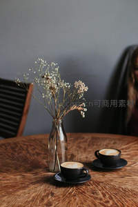 木质桌上的双杯拿铁与干花瓶，柔和光影营造温馨咖啡馆氛围