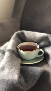 灰调毛毯包裹下的青瓷茶杯，盛满红茶，温馨居家慢生活写照