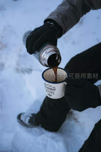 雪地中戴手套的人正将热咖啡倒入印有文字的搪瓷杯