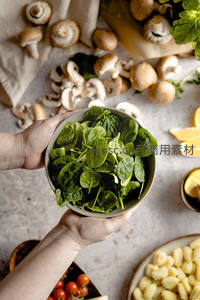双手捧碗新鲜菠菜，周围散落蘑菇与意式土豆团子