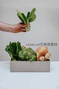 手举上海青，纸盒内盛放西兰花、南瓜与姜，简约有机蔬果配送场景