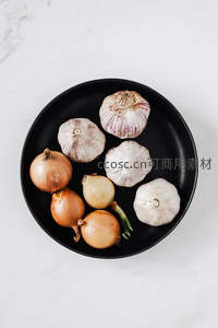 黑盘盛放洋葱与大蒜俯拍图，简约大理石背景凸显食材本真