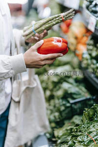 双手挑选红甜椒与芦笋，超市生鲜区光影交错，突出食材新鲜与选购瞬间