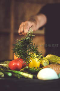 手撒迷迭香于烤盘蔬果上，番茄彩椒玉米鱼片热气氤氲，烹饪进行时