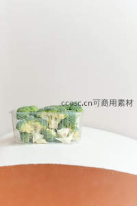 透明盒装西兰花静置于纯白桌面，极简主义食材摄影